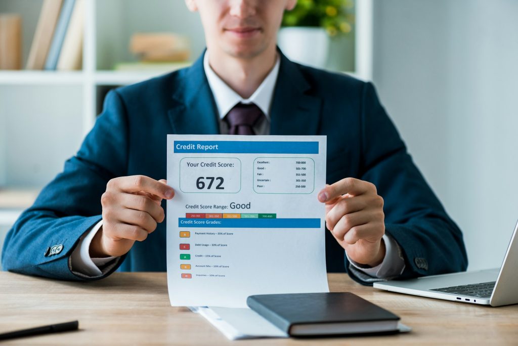 selective focus of man holding document with credit report lettering near laptop in office